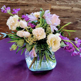 Low arrangement of peach roses and carnations with purple flowers in a clear glass cube vase