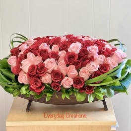 Oval arrangement of red and pink roses in a low wooden container