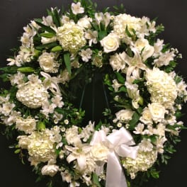 White floral wreath with a satin ribbon bow on a dark background