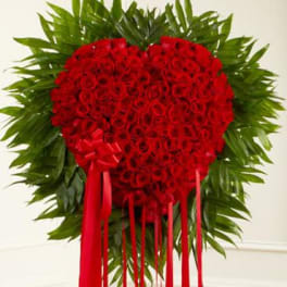 Heart-shaped red rose arrangement with green foliage and red ribbons