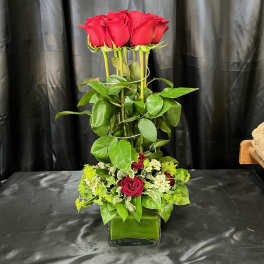 Tall arrangement of red roses in a glass vase with a low cluster of mixed flowers