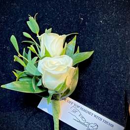White rose boutonniere with green leaves on a tag