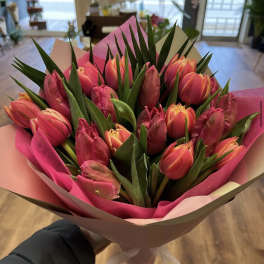 Hand-tied bouquet of pink and orange tulips with tall green foliage in pink and cream wrapping paper.