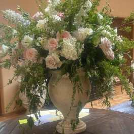 Large urn arrangement with white and blush flowers and cascading greenery on a round wooden table
