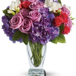 Mixed bouquet of purple, pink, red, and white flowers in a clear glass vase