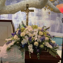 Large funeral flower arrangement with white and purple blooms beneath a crucifix