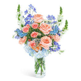 Peach roses and blue flowers in a clear glass vase with butterfly picks