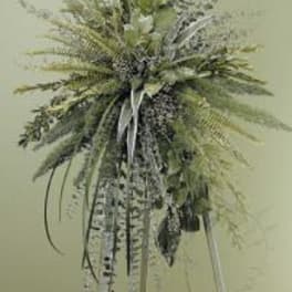 Tall standing arrangement of cascading mixed greenery on a pale backdrop