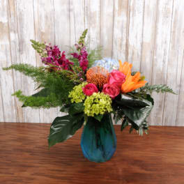 Bright mixed arrangement with pink roses, orange lilies, and green hydrangea in a blue glass vase