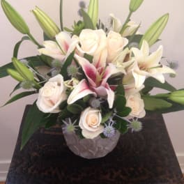 Compact arrangement of cream roses and pink lilies in a gray textured vase on a dark wooden table
