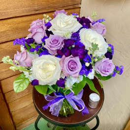 Bouquet of white, lavender, and purple roses in a glass vase with a purple ribbon