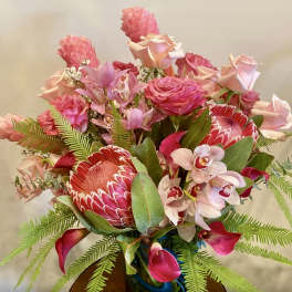 Pink and red tropical bouquet with roses, orchids, and protea in a vase