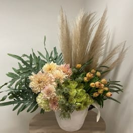 Tall asymmetrical arrangement with peach dahlias, green blooms, yellow tulips and pampas plumes in a white pot
