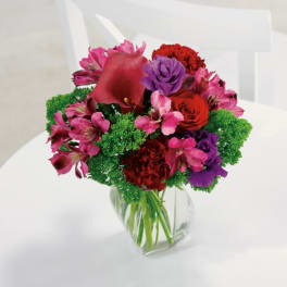 Vibrant bouquet of red, pink, and purple flowers with bright green accents in a clear glass vase
