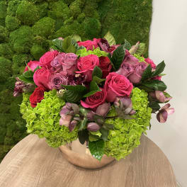 Low round arrangement of hot pink and mauve roses with green hydrangeas in a metallic bowl vase