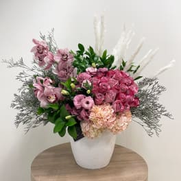 Large pink rose, orchid, hydrangea and lisianthus arrangement in a white pot with pampas plumes