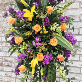 Standing floral spray with orange roses, yellow lilies, and purple blooms