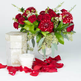 Red roses and red-white dahlias in a glass vase with rose petals