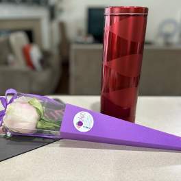 Single pale pink rose in a purple cone wrap beside a red cylindrical gift tin