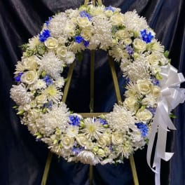 White floral wreath with blue accents on a wooden easel and white ribbon