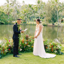 Bride and groom standing by tropical floral arrangements during a wedding ceremony