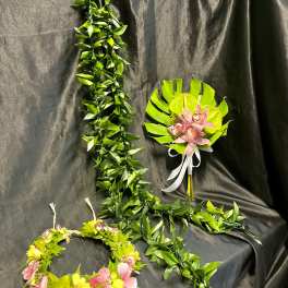Two floral leis and a pink orchid bouquet on a dark draped background.