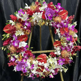 Large floral wreath with orchids, anthuriums, and red tropical blooms on a stand