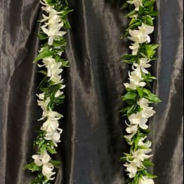 White floral lei with green leaves on dark fabric