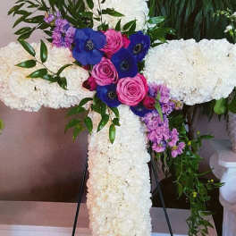 White floral cross on an easel with pink and blue flowers at the center