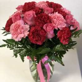 Arrangement of pink roses and red and pink carnations in a clear vase with a pink ribbon