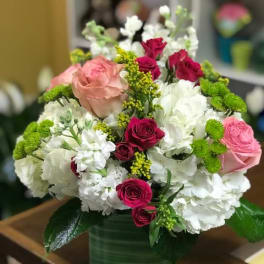 Round arrangement of white hydrangeas with pink and red roses in a green glass cube vase
