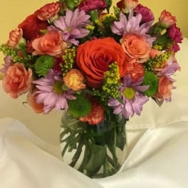 Mixed bouquet of roses, carnations, and purple daisies in a glass vase