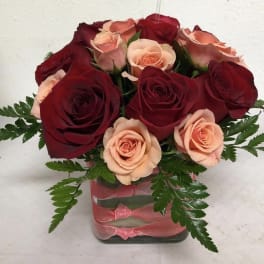 Bouquet of red and peach roses in a square glass vase with pink ribbon