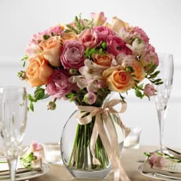Pink and peach roses and ranunculus in a clear glass vase with a ribbon bow