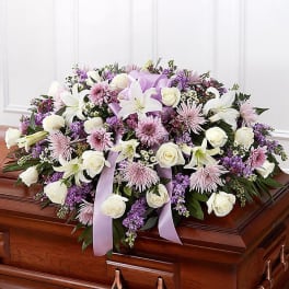Lavender and white casket spray with roses, lilies, and mums on a wooden casket.