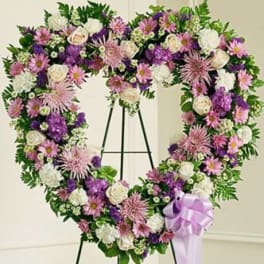 Heart-shaped standing wreath with purple, pink, and white flowers and a lavender ribbon bow