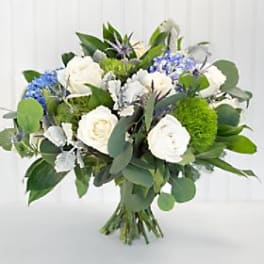 Hand-tied bouquet of white roses, blue hydrangeas, and green pom flowers in a rounded shape