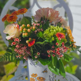 Mixed bouquet in a painted white mug with orange and pink flowers.