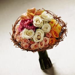 Hand-tied bouquet of cream, peach, and orange roses with calla lilies, wrapped in a twig collar.