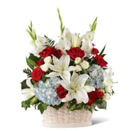 Patriotic basket arrangement with white lilies, red roses, and light blue hydrangeas in a white woven basket