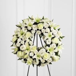 White standing wreath of lilies, roses, and mums on a black easel