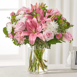 Pink lilies and roses arranged in a clear glass vase