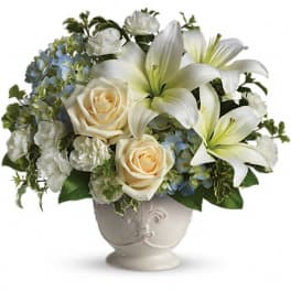 White lilies and cream roses in a decorative vase with blue hydrangeas