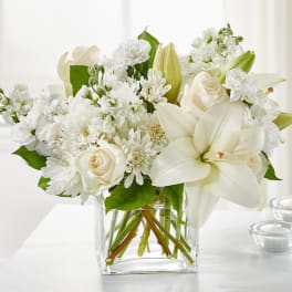 White floral arrangement in a clear glass vase with roses and lilies