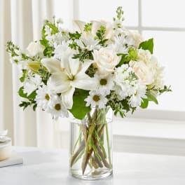 White roses, lilies, and daisies arranged in a clear glass vase
