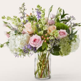 Pastel bouquet of roses, hydrangeas, and purple flowers in a clear glass vase