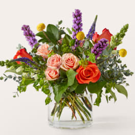 Mixed bouquet of roses and purple spikes in a clear glass vase