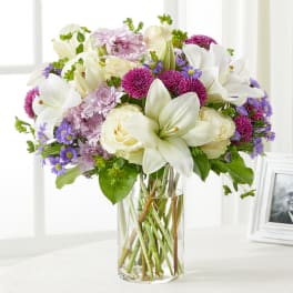 Bouquet of white lilies, cream roses, and purple flowers in a glass vase