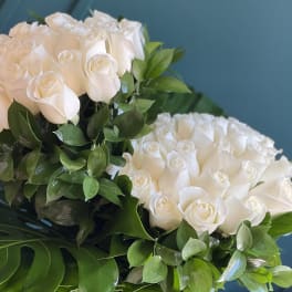 Two bouquets of white roses with green foliage against a blue background