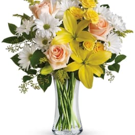 Yellow lilies, peach roses, and white daisies in a clear glass vase